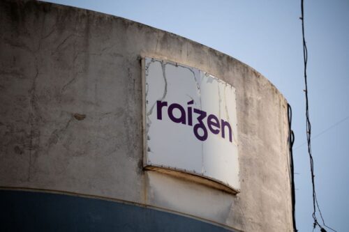 Fotografia em close do logotipo da Raízen, em letras roxas sobre uma placa branca levemente desgastada.