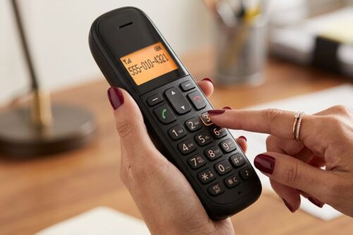 Close das mãos de uma pessoa discando um número em um telefone sem fio preto de design clássico sobre uma mesa de escritório.