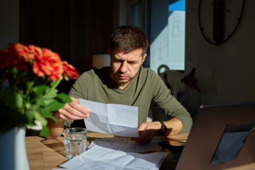 Homem sentado à mesa com laptop e papéis, representando a pesquisa Datafolha sobre busca por renda extra.