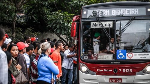Passageiros aguardam ônibus lotado em São Paulo durante feriado do Dia do Trabalho, com mudanças no transporte público.