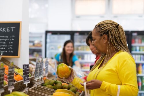 Consumidora escolhe frutas no mercado, refletindo alta de preços e inflação medida pelo IPC-S da FGV.