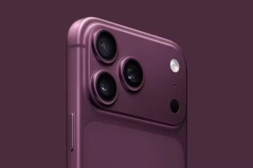 Vista em close-up da parte traseira superior de um smartphone (estilo iPhone) na cor "Dark Cherry" (um tom de roxo profundo e sofisticado). O destaque é o módulo de câmeras triplas dispostas em um relevo quadrado com bordas arredondadas. O acabamento do corpo é fosco, enquanto os anéis das lentes têm um brilho metálico sutil. O fundo é de uma cor sólida que combina com o tom do aparelho, criando uma estética minimalista e moderna.
