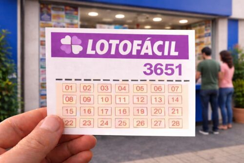 Pessoa segura volante da Lotofácil 3651 em frente a uma lotérica, com clientes ao fundo aguardando atendimento.