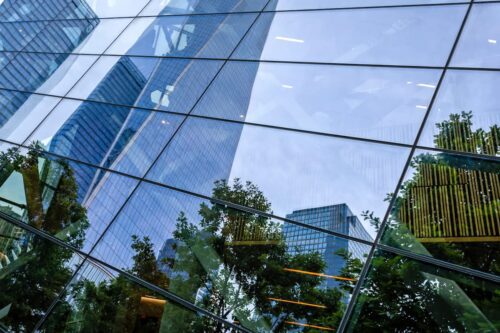 Fachada de prédio corporativo com vidro refletindo árvores e arranha-céus, representando o mercado de fundos imobiliários.
