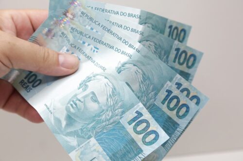 Mão segurando notas de R$100, representando juros altos e impacto da Selic nas taxas do Tesouro Direto.