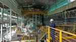 Interior de usina siderúrgica da Usiminas (USIM5), com operador e equipamentos industriais em operação.