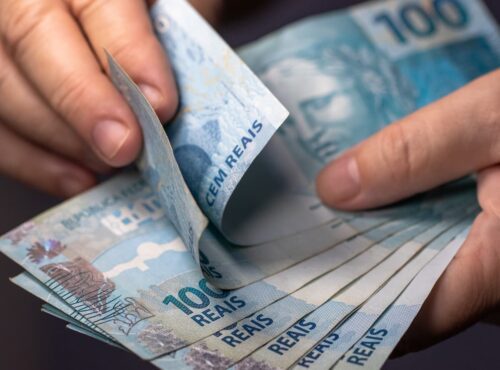 Pessoa conta cédulas de real; milhões ainda têm valores a receber esquecidos em bancos, segundo o Banco Central.