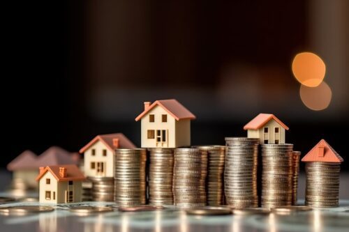 Miniaturas de casas sobre pilhas de moedas, simbolizando fundos imobiliários e pagamento de dividendos na semana.