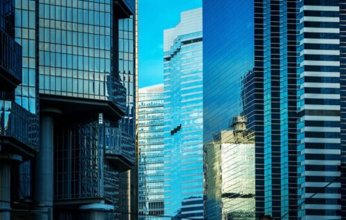 Rua da cidade com prédios altos sob um céu azul, representando o ambiente urbano dos fundos imobiliários (FIIs).