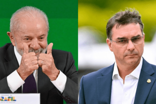 Imagem dividida verticalmente ao meio, mostrando dois homens da política brasileira em planos médios. À esquerda, o presidente Luiz Inácio Lula da Silva, um homem idoso de cabelos e barba grisalhos, sorri e faz um gesto de positivo com os dois polegares levantados; ele veste terno escuro, camisa branca e gravata roxa, tendo ao fundo uma parede verde. À direita, o senador Flávio Bolsonaro, um homem de cabelos escuros e óculos de grau, aparece com uma expressão séria e olhar focado; ele veste um paletó azul-marinho sobre camisa branca, com um fundo verde e amarelo desfocado.