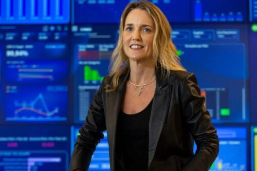 Retrato da executiva Claudia Woods, ex-CEO da Uber Brasil. Ela está posicionada no centro, vestindo uma jaqueta de couro preta.