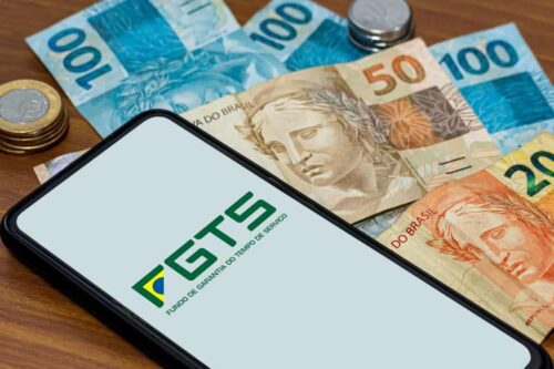 Um smartphone sobre uma mesa de madeira exibindo o logotipo do FGTS (Fundo de Garantia do Tempo de Serviço) na tela.