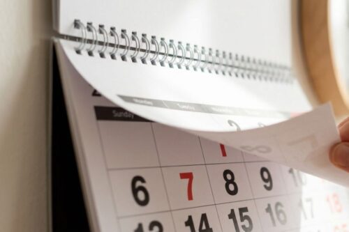 Uma mão com dois anéis, um simples e um duplo, vira a página de um calendário de parede espiral.