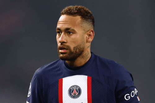 Uma imagem em plano médio centraliza o jogador de futebol Neymar Jr. do peito para cima, olhando ligeiramente para a esquerda com uma expressão séria e concentrada. Ele tem pele parda, barba curta e bem aparada, e cabelo castanho curto, raspado nas laterais em estilo fade (degradê) e texturizado no topo.