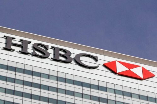 Vista em ângulo baixo da fachada de um edifício corporativo moderno com o logotipo do banco HSBC e seu símbolo de hexágono vermelho e branco no topo.
