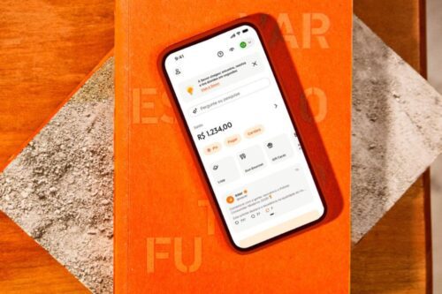 Um smartphone sobre um livro de capa laranja exibe a interface do aplicativo do Banco Inter.