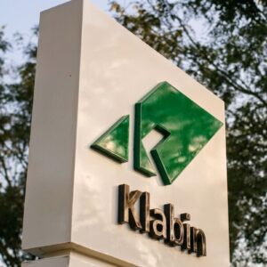 Totem branco de sinalização externa com o logotipo verde da Klabin e o nome da empresa em letras pretas.
