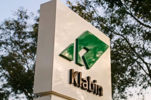 Totem branco de sinalização externa com o logotipo verde da Klabin e o nome da empresa em letras pretas.