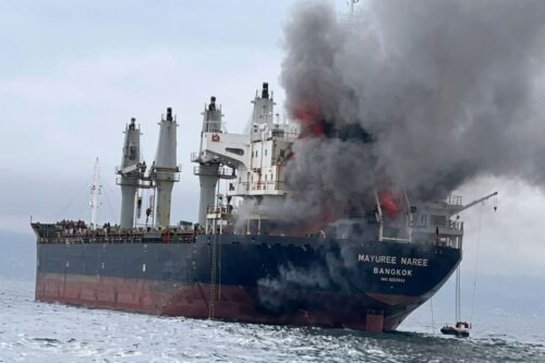 Navio cargueiro de grande porte chamado "Mayuree Naree" em alto-mar, com uma densa coluna de fumaça cinza e preta saindo da parte central da embarcação devido a um incêndio.