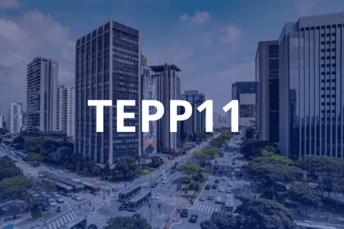 Imagem aérea de uma grande avenida movimentada com prédios comerciais e tráfego de veículos. Sobreposta ao centro da imagem, destaca-se a inscrição "TEPP11" em letras maiúsculas brancas. Todo o fundo possui um filtro azulado.