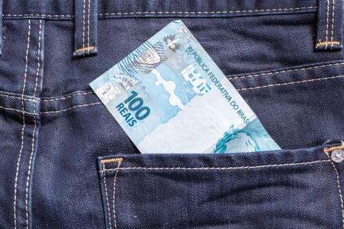 Nota de R$ 100 no bolso de uma calça jeans, representando dinheiro e finanças pessoais após bloqueio judicial.