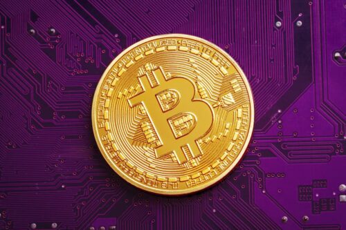 Moeda de bitcoin dourada sobre placa eletrônica roxa em referência ao Bitcoin Pizza Day e criptomoedas no Nubank.