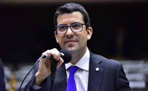 Deputado Marcelo Queiroz fala ao microfone na Câmara; PF investiga suspeita de fraude em contratos milionários.
