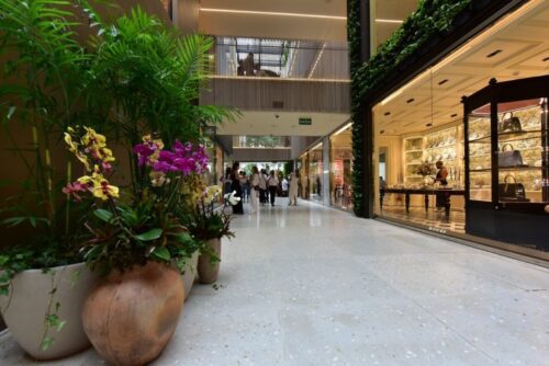 Vista do shopping Shops Jardins, um shopping de alto luxo em São Paulo, destacando a vegetação e flores que embelezam o espaço interno e presentando a venda da parte do FII XP Malls.