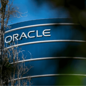 Foto em ângulo contra-plongée mostrando o topo de um edifício comercial cilíndrico de vidro azul com o logotipo da empresa "ORACLE" em letras maiúsculas brancas. Galhos de árvores desfocados aparecem em primeiro plano nas laterais.