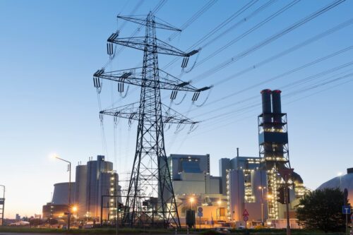 Linhas de transmissão de energia e usina elétrica ao entardecer, setor de infraestrutura e geração de energia.