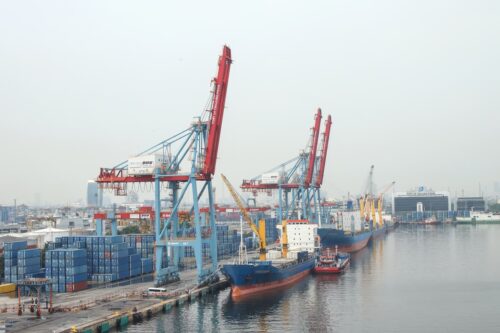 Navios cargueiros atracados em porto com contêineres e guindastes, ilustrando exportações e comércio exterior brasileiro.