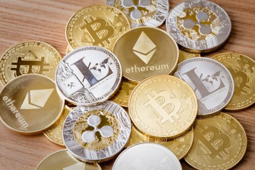 Moedas físicas de Bitcoin, Ethereum, Litecoin e Ripple espalhadas sobre superfície de madeira.
