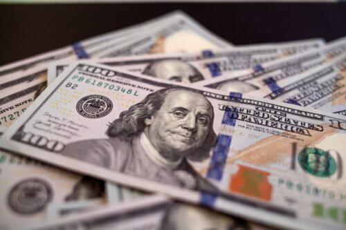 Notas de dólar americano de 100 dólares espalhadas, representando câmbio, mercado financeiro e valorização da moeda.