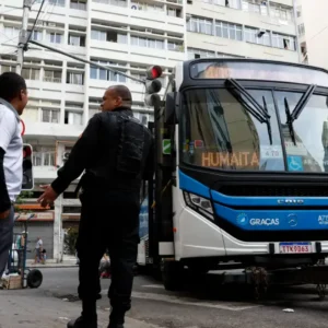 Ônibus parado durante a greve dos rodoviários no Rio de Janeiro, com passageiros e agente de segurança na rua.