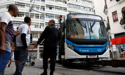 Ônibus parado durante a greve dos rodoviários no Rio de Janeiro, com passageiros e agente de segurança na rua.