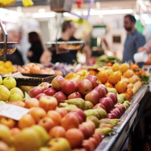 Bancas de frutas e legumes em mercado, ilustrando preços de alimentos e inflação ao consumidor.