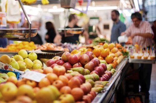 Bancas de frutas e legumes em mercado, ilustrando preços de alimentos e inflação ao consumidor.