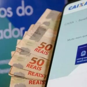 Celular exibe consulta ao PIS ao lado de notas de real, ilustrando pagamento do abono salarial.