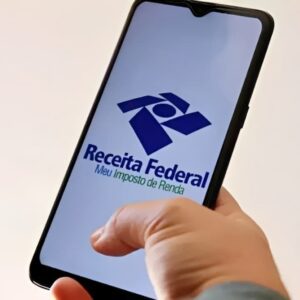 Pessoa segura celular com aplicativo Meu Imposto de Renda da Receita Federal aberto na tela.