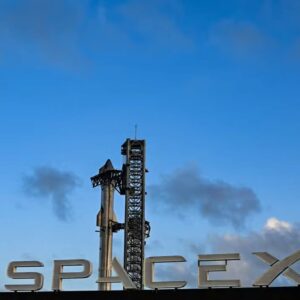 Foguete Starship da SpaceX em plataforma de lançamento, com estrutura metálica ao fundo sob céu azul.