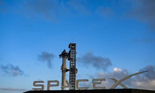 Foguete Starship da SpaceX em plataforma de lançamento, com estrutura metálica ao fundo sob céu azul.