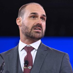 Eduardo Bolsonaro fala em evento, usando terno e gravata, durante participação em conferência nos Estados Unidos.