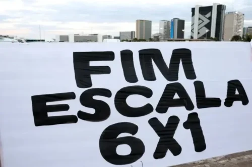 Uma faixa branca estendida horizontalmente exibe a frase "FIM ESCALA 6X1" escrita em grandes letras pretas e maiúsculas. Ao fundo, sob um céu nublado, é possível ver uma área aberta com prédios urbanos e a arquitetura característica de Brasília, incluindo o edifício do Banco do Brasil.