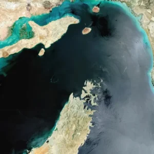 Imagem de satélite do Estreito de Ormuz, mostrando a Península de Musandam ao sul e a costa do Irã ao norte, com águas em tons de azul-escuro e turquesa que conectam o Golfo Pérsico ao Golfo de Omã.