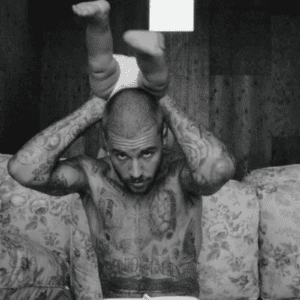 Uma foto em preto e branco de Justin Bieber, sem camisa e exibindo suas diversas tatuagens no peito e nos braços. Ele está posicionado atrás de um sofá com estampa floral, olhando diretamente para a câmera. Ele segura um bebê pelas pernas, que está de cabeça para baixo acima de sua cabeça, com as pernas para o ar vestindo uma fralda. O fundo possui uma parede texturizada de madeira.