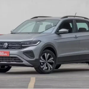 Volkswagen T-Cross cinza prateado visto de frente e em ângulo. O SUV compacto apresenta grade dianteira cromada com o logo da VW ao centro, faróis em LED, rodas de liga leve diamantadas e rack de teto preto. Na placa dianteira há um adesivo vermelho com o logotipo da revista Autoesporte.