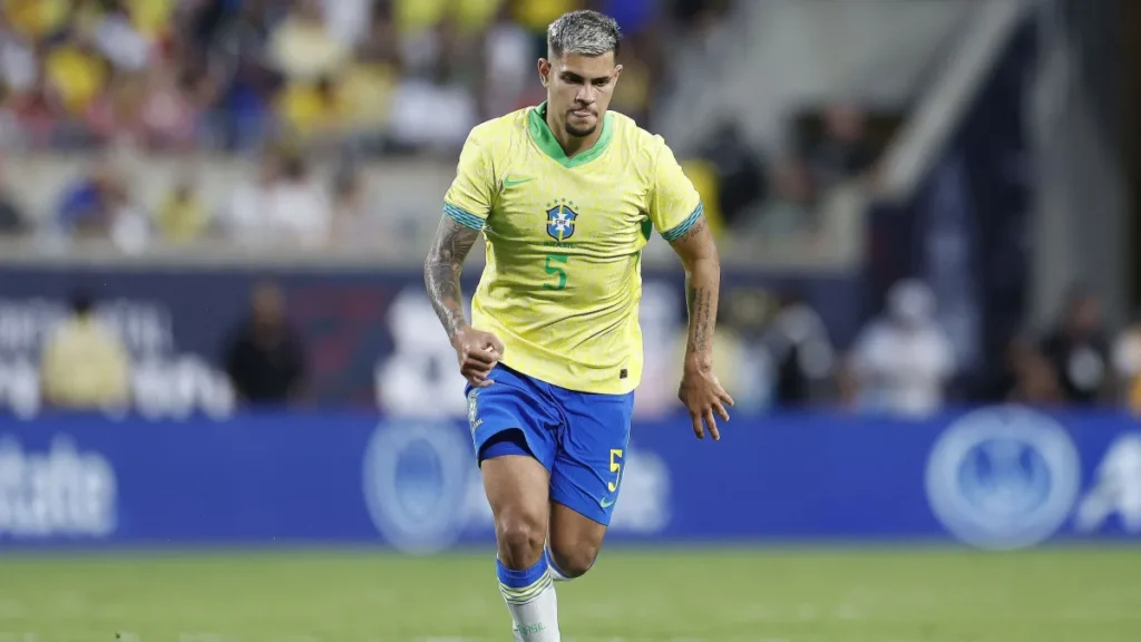 Bruno Guimarães corre com a camisa da Seleção Brasileira durante partida em estádio de futebol.