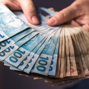 Pessoa segura e conta notas de R$ 100, representando restituição do Imposto de Renda e pagamento ao contribuinte.