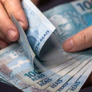 Pessoa segura e conta notas de R$ 100, ilustrando tema sobre crédito consignado e finanças.