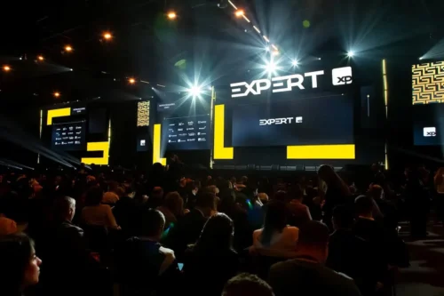 Palco da Expert XP 2026 com palestrantes e plateia acompanhando apresentações sobre investimentos e economia.